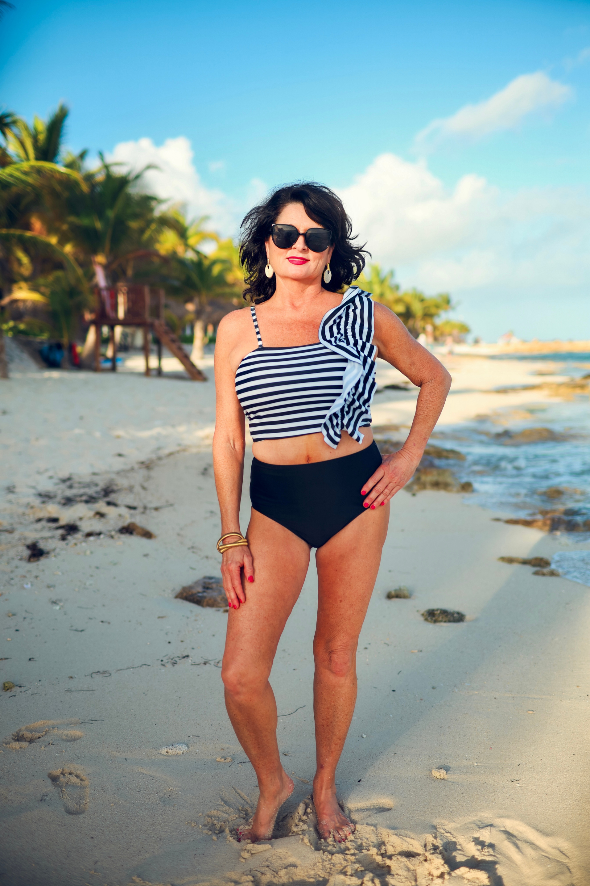 a two-piece swimsuit sold separately made of stretchy material with a black and white striped crop top, one chunky ruffle strap, one adjustable removable spaghetti strap, and coordinating solid black high-waisted bottoms