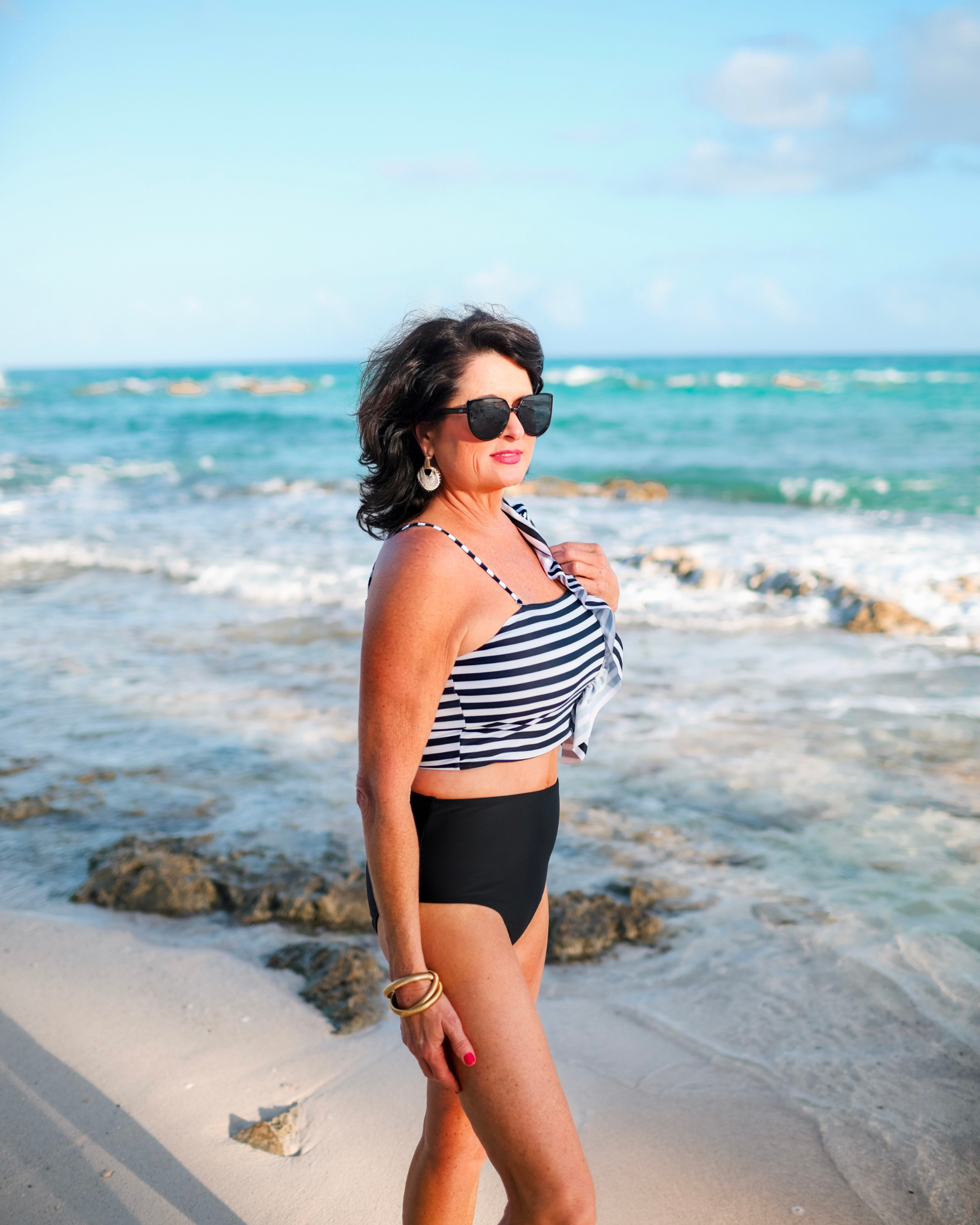 a two-piece swimsuit sold separately made of stretchy material with a black and white striped crop top, one chunky ruffle strap, one adjustable removable spaghetti strap, and coordinating solid black high-waisted bottoms
