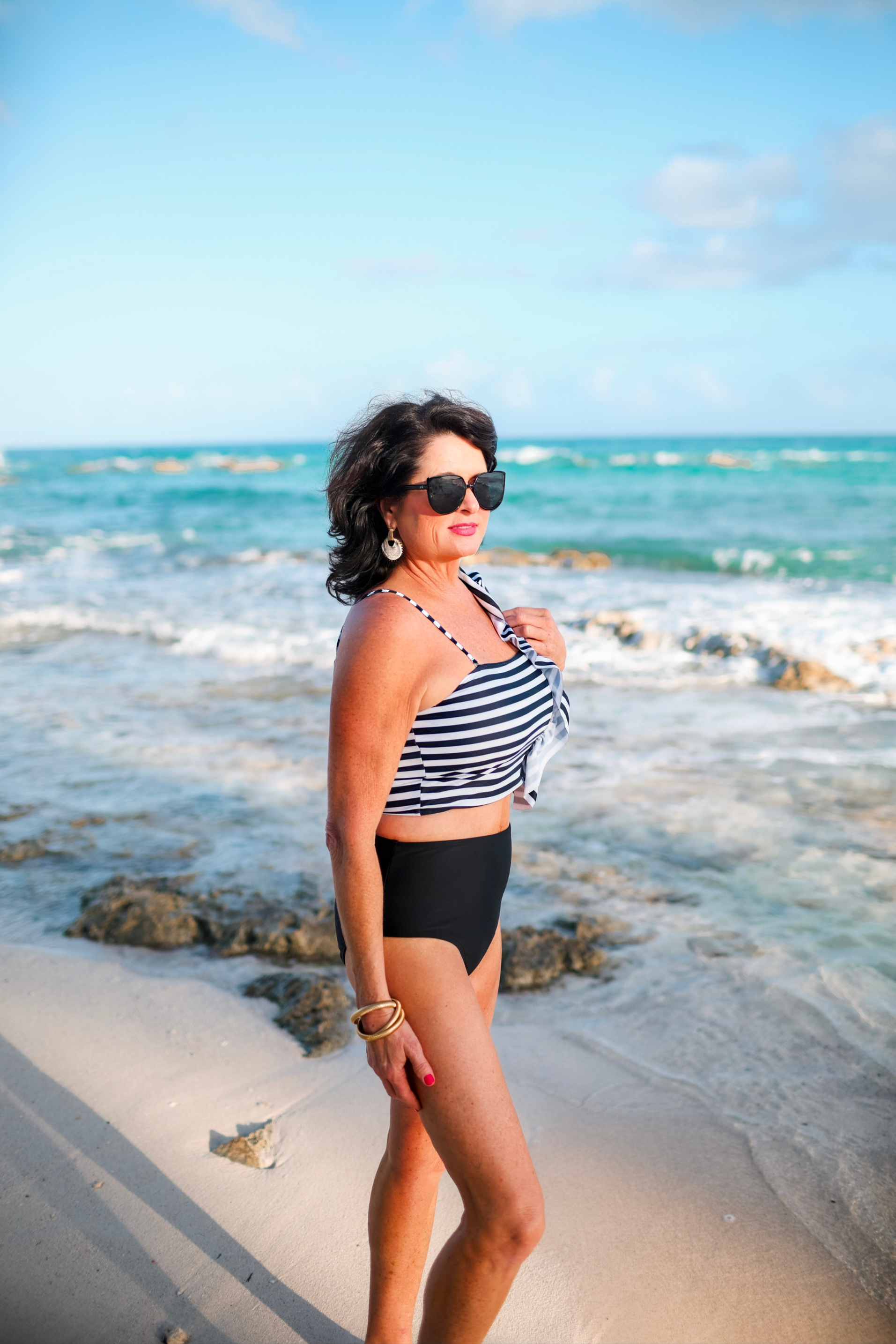 a two-piece swimsuit sold separately made of stretchy material with a black and white striped crop top, one chunky ruffle strap, one adjustable removable spaghetti strap, and coordinating solid black high-waisted bottoms