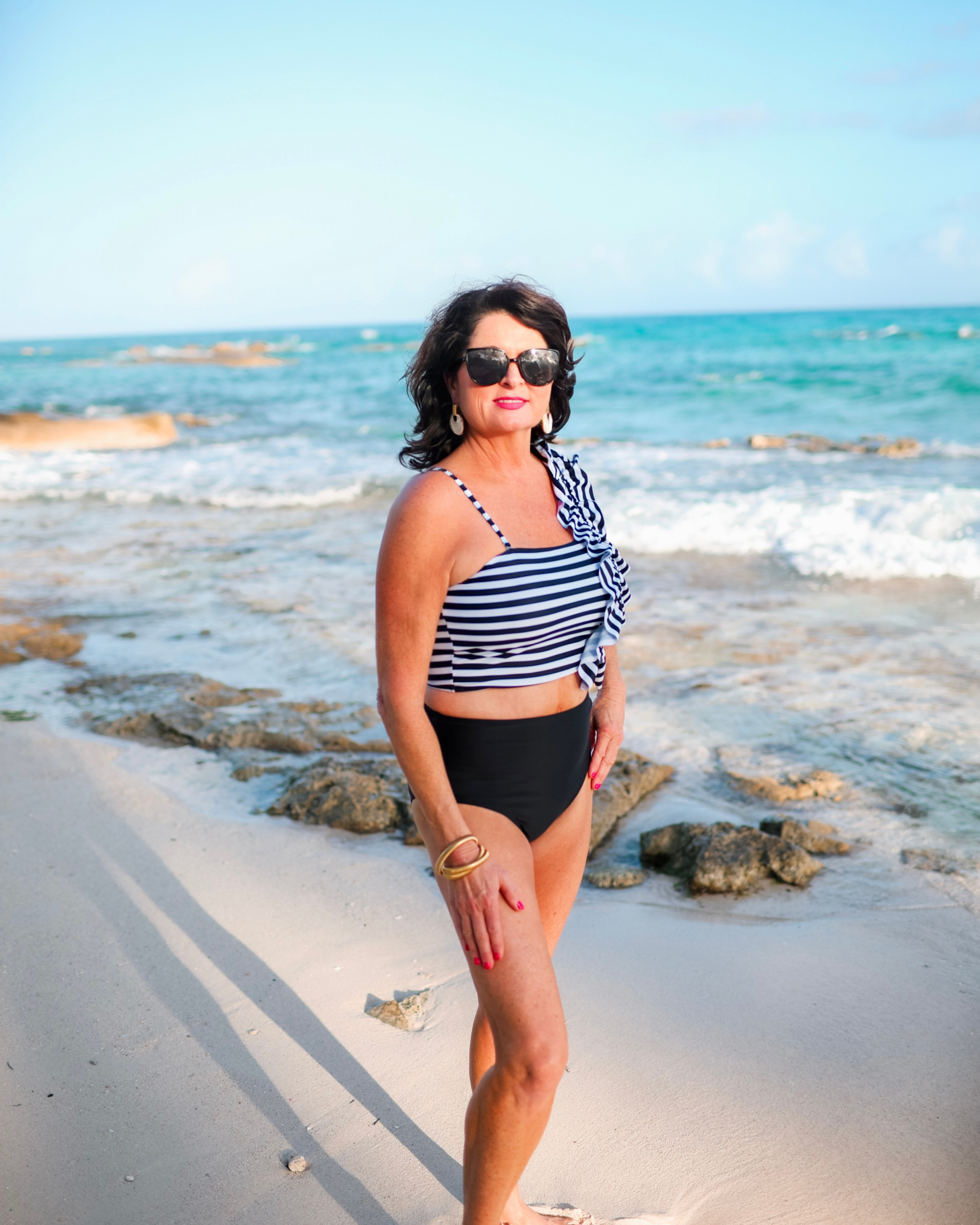 a two-piece swimsuit sold separately made of stretchy material with a black and white striped crop top, one chunky ruffle strap, one adjustable removable spaghetti strap, and coordinating solid black high-waisted bottoms