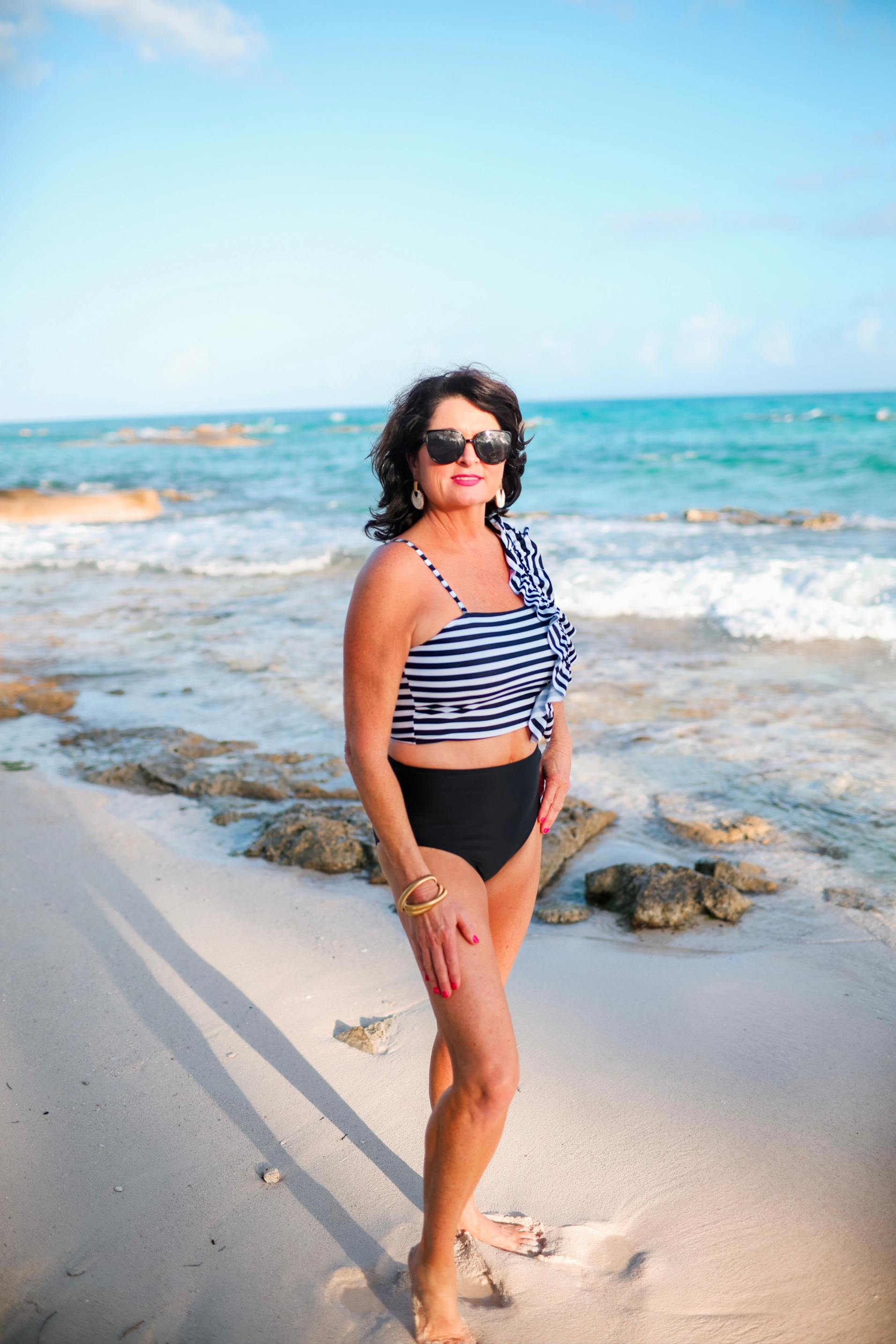 a two-piece swimsuit sold separately made of stretchy material with a black and white striped crop top, one chunky ruffle strap, one adjustable removable spaghetti strap, and coordinating solid black high-waisted bottoms