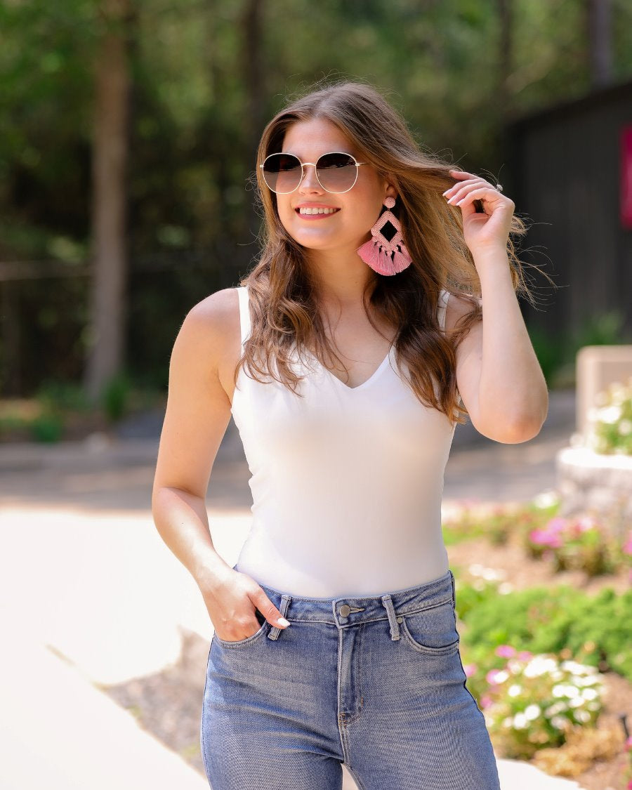 one-piece bodysuit made of soft and stretchy lightweight material with a v-neckline, sleeveless shoulder straps with a racerback fit, and a form-fitting silhouette that falls into a cheeky fit with a snap button closure in ivory