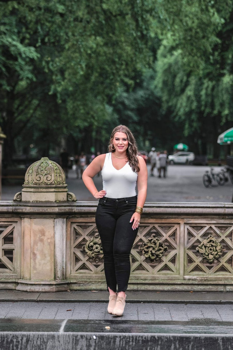 an ivory one-piece bodysuit made from soft stretchy lightweight material with a V-neckline, sleeveless shoulder straps, racerback fit, form-fitting silhouette, cheeky fit bottoms, and a snap-button closure