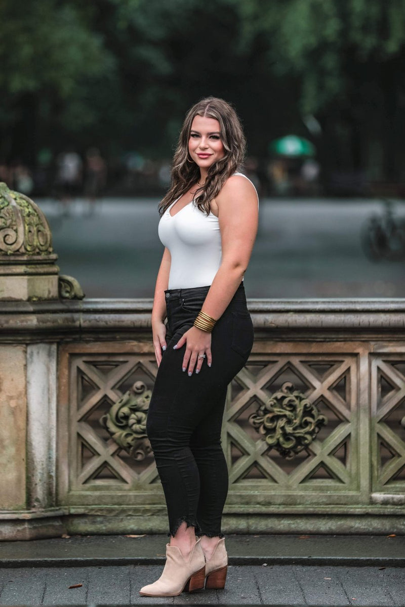 an ivory one-piece bodysuit made from soft stretchy lightweight material with a V-neckline, sleeveless shoulder straps, racerback fit, form-fitting silhouette, cheeky fit bottoms, and a snap-button closure