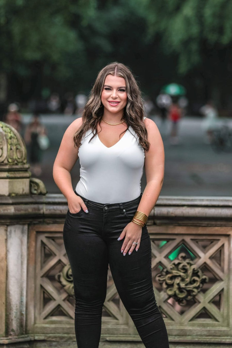an ivory one-piece bodysuit made from soft stretchy lightweight material with a V-neckline, sleeveless shoulder straps, racerback fit, form-fitting silhouette, cheeky fit bottoms, and a snap-button closure