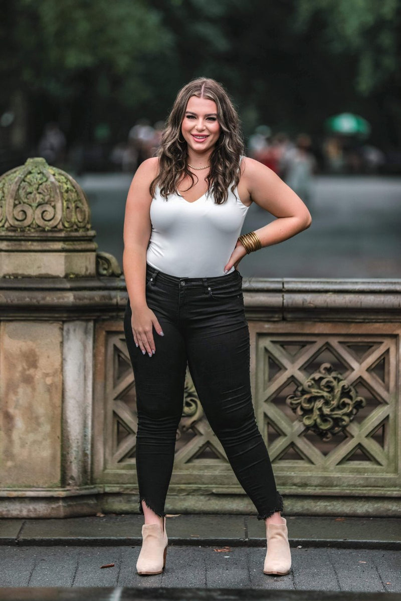 an ivory one-piece bodysuit made from soft stretchy lightweight material with a V-neckline, sleeveless shoulder straps, racerback fit, form-fitting silhouette, cheeky fit bottoms, and a snap-button closure