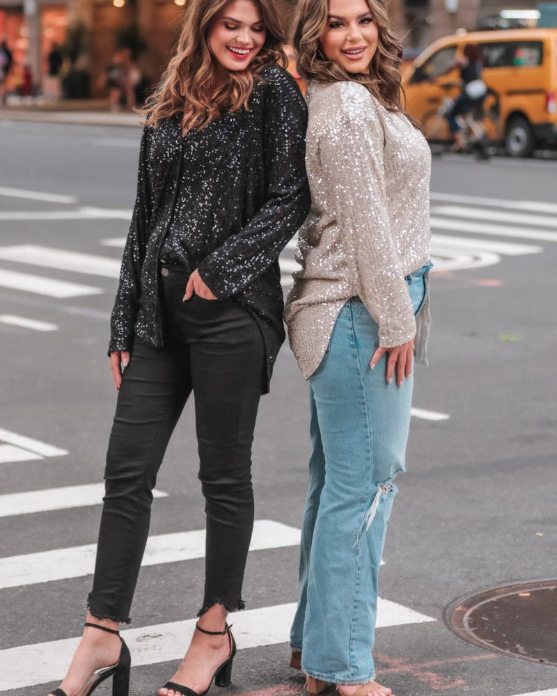 a loose long-sleeve top made of lightweight material covered in shimmering sequins with a collared neckline, fitted button closure cuffs, an accent chest pocket, and a relaxed button-up silhouette that falls into a round high-low hemline in black and champagne