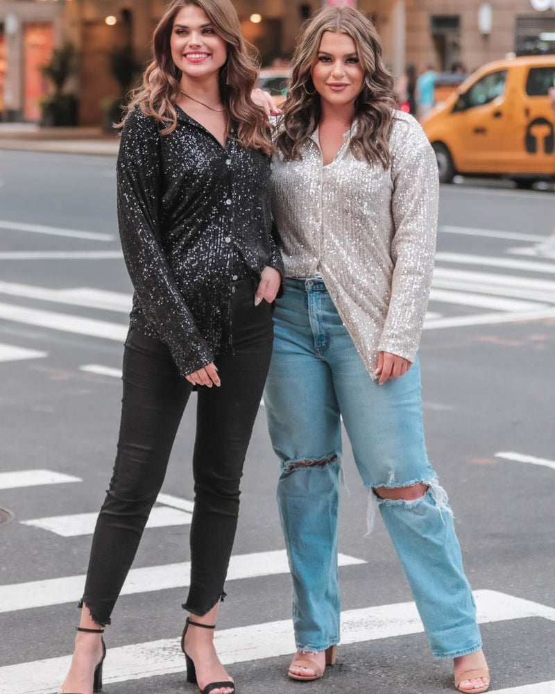 a loose long-sleeve top made of lightweight material covered in shimmering sequins with a collared neckline, fitted button closure cuffs, an accent chest pocket, and a relaxed button-up silhouette that falls into a round high-low hemline in black and champagne