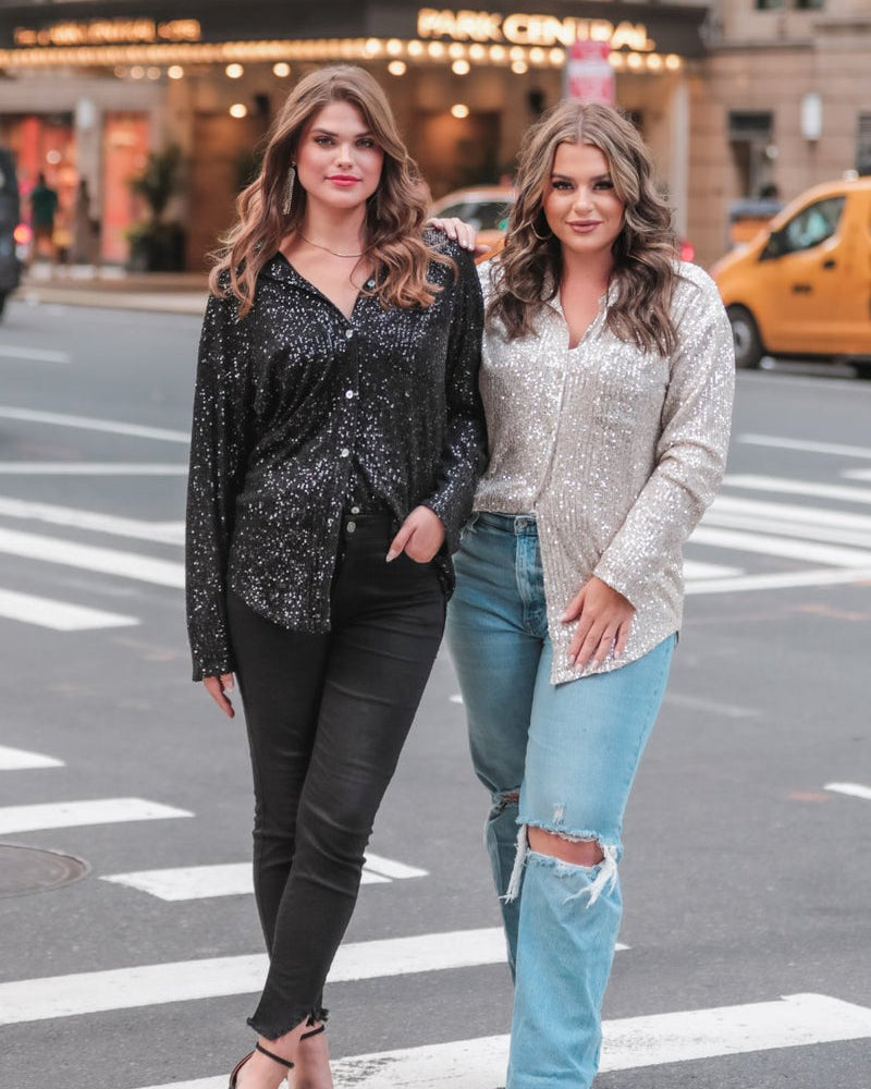 a loose long-sleeve top made of lightweight material covered in shimmering sequins with a collared neckline, fitted button closure cuffs, an accent chest pocket, and a relaxed button-up silhouette that falls into a round high-low hemline in black and champagne