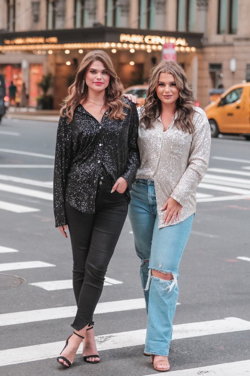 a loose long-sleeve top made of lightweight material covered in shimmering sequins with a collared neckline, fitted button closure cuffs, an accent chest pocket, and a relaxed button-up silhouette that falls into a round high-low hemline in black and champagne