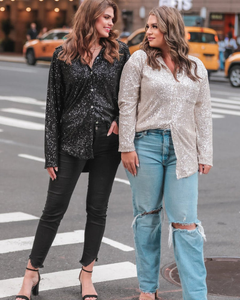 a loose long-sleeve top made of lightweight material covered in shimmering sequins with a collared neckline, fitted button closure cuffs, an accent chest pocket, and a relaxed button-up silhouette that falls into a round high-low hemline in black and champagne