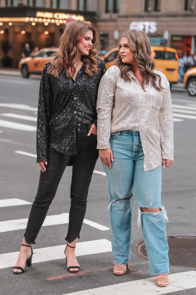 a loose long-sleeve top made of lightweight material covered in shimmering sequins with a collared neckline, fitted button closure cuffs, an accent chest pocket, and a relaxed button-up silhouette that falls into a round high-low hemline in black and champagne