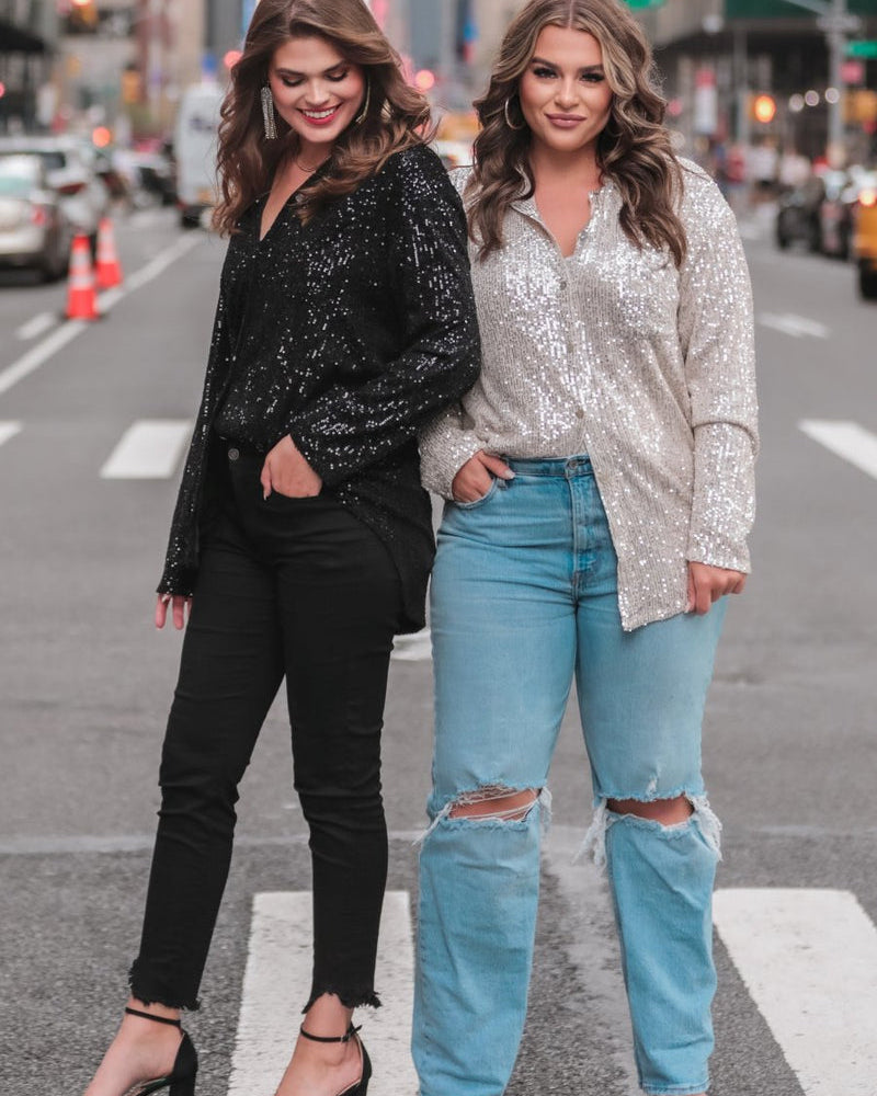 a loose long-sleeve top made of lightweight material covered in shimmering sequins with a collared neckline, fitted button closure cuffs, an accent chest pocket, and a relaxed button-up silhouette that falls into a round high-low hemline in black and champagne