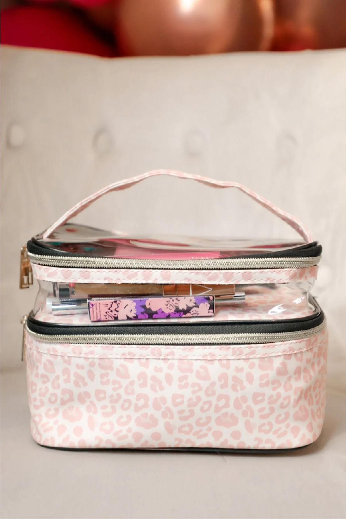 two-tier design with a clear compartment, four brush slots with an elastic band on the inside lid of the main compartment, and a grab-and-go handle with dual gold zippers in a soft pink animal print on ivory background 
