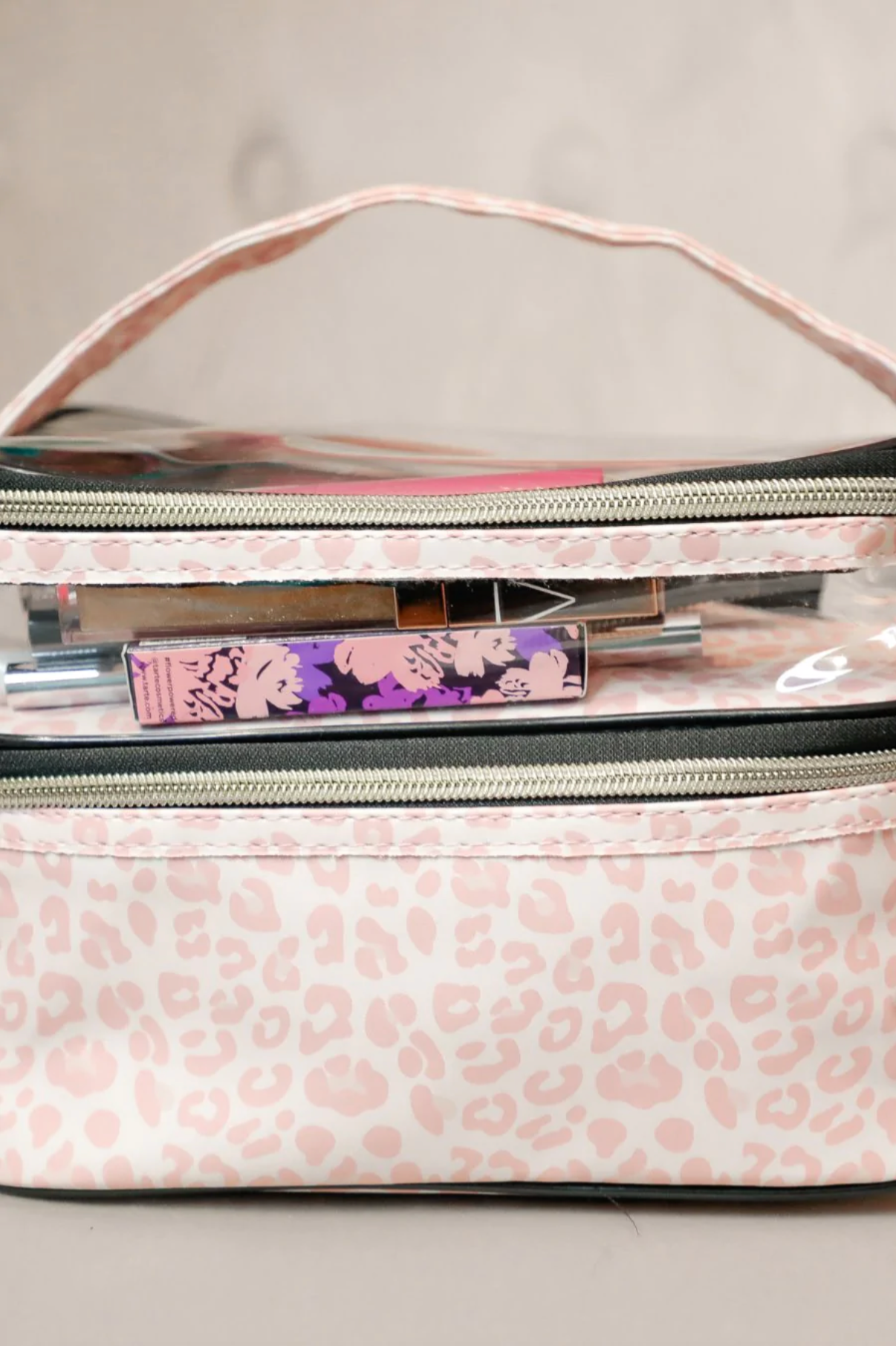 two-tier design with a clear compartment, four brush slots with an elastic band on the inside lid of the main compartment, and a grab-and-go handle with dual gold zippers in a soft pink animal print on ivory background 