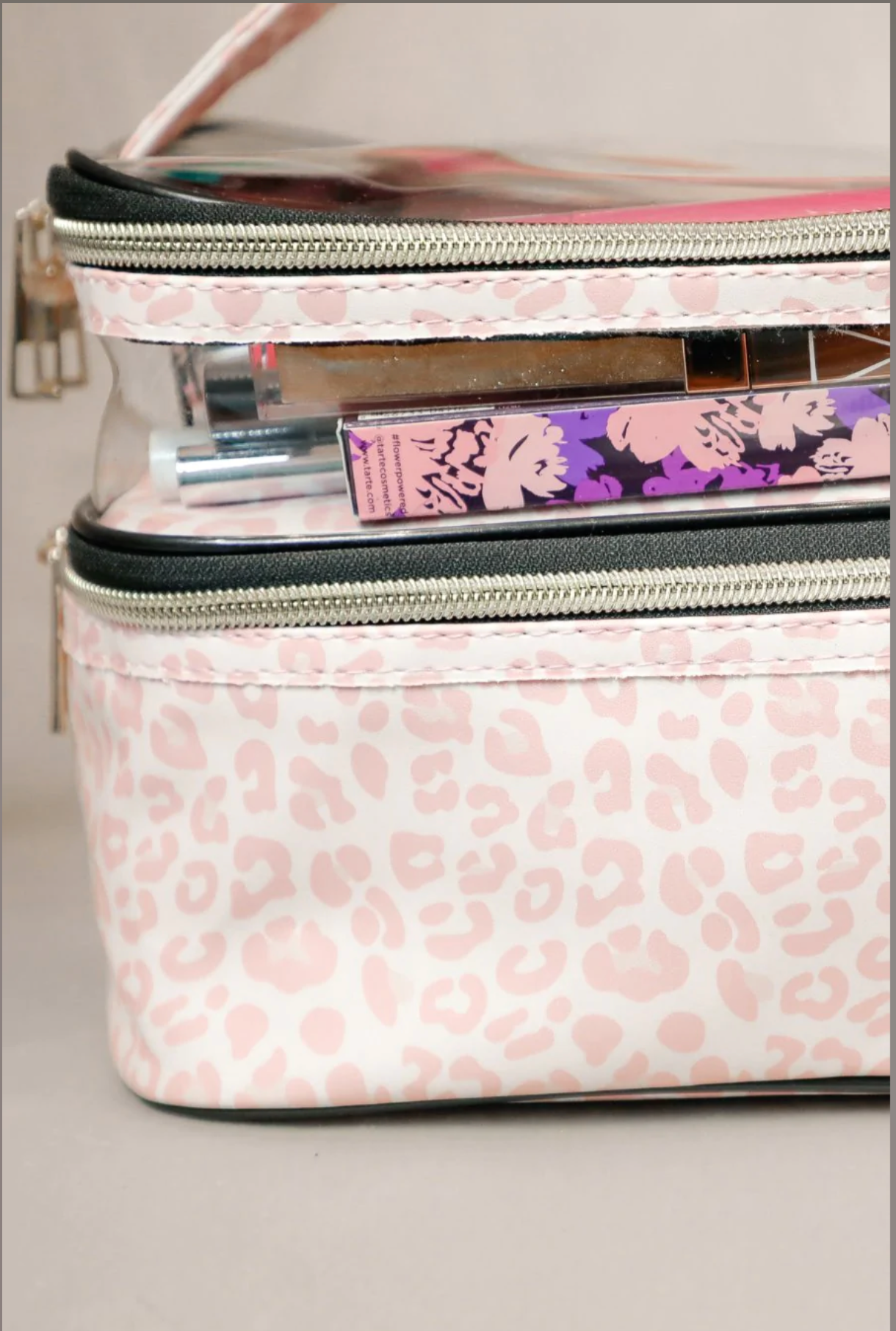 two-tier design with a clear compartment, four brush slots with an elastic band on the inside lid of the main compartment, and a grab-and-go handle with dual gold zippers in a soft pink animal print on ivory background 