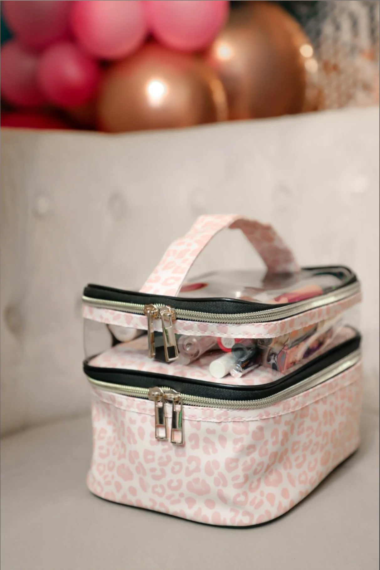 two-tier design with a clear compartment, four brush slots with an elastic band on the inside lid of the main compartment, and a grab-and-go handle with dual gold zippers in a soft pink animal print on ivory background 