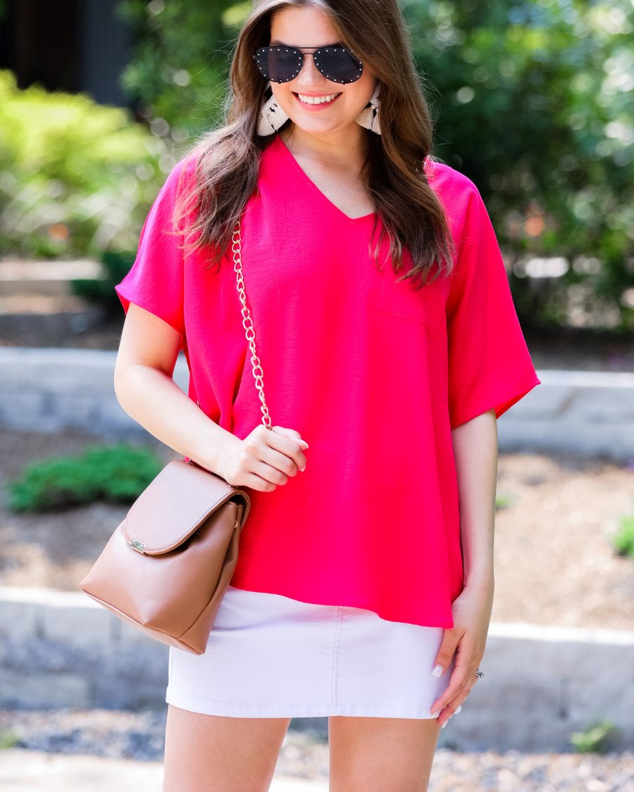 a lightweight magenta short-sleeve woven tunic with a V-neckline, a front chest pocket, and a relaxed, non-stretch silhouette