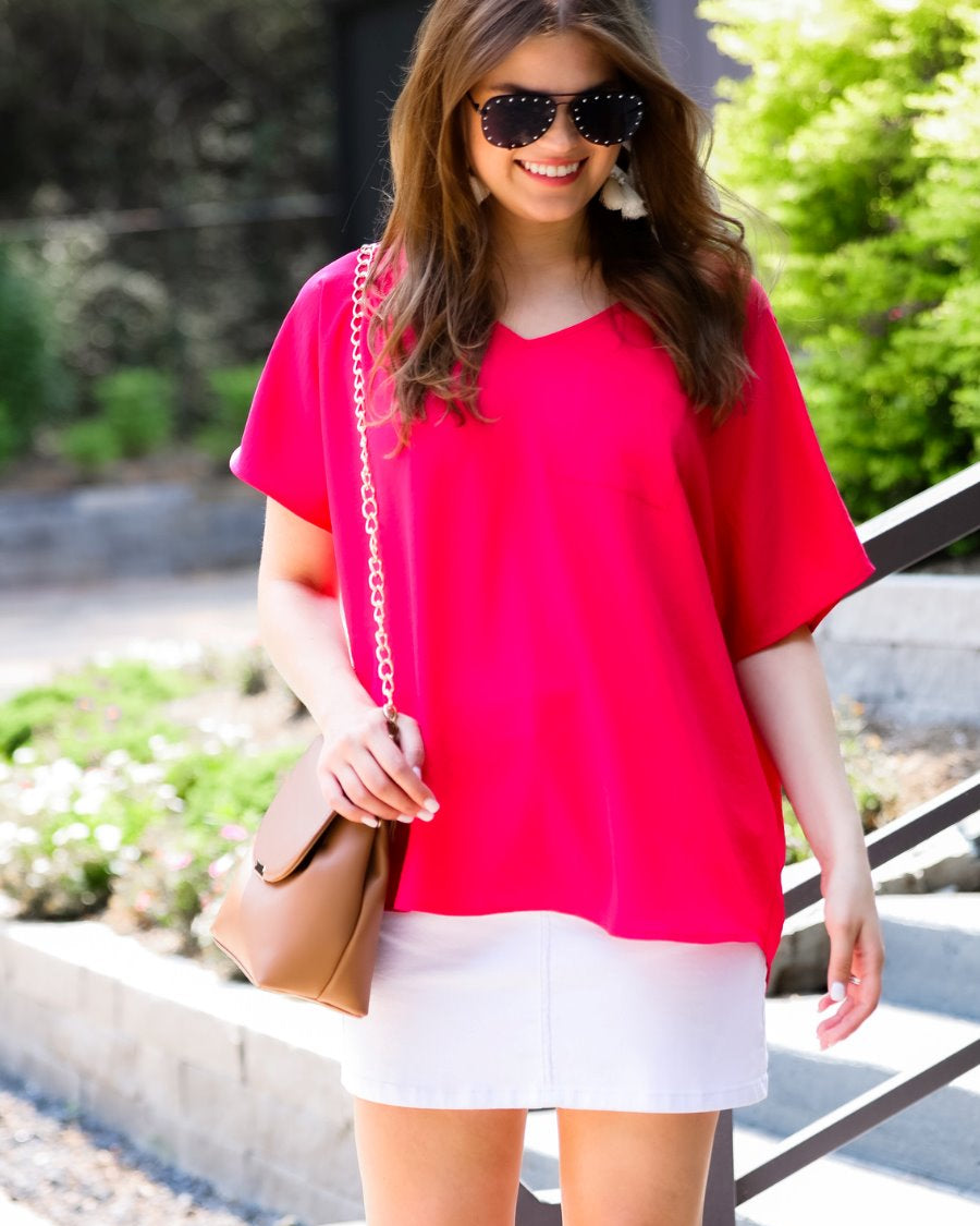 a lightweight magenta short-sleeve woven tunic with a V-neckline, a front chest pocket, and a relaxed, non-stretch silhouette