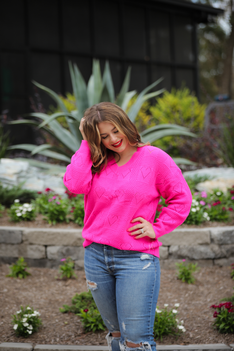 a pink long-sleeve open-knit sweater with a cutout heart pattern and ribbed detailing on the V-neckline, cuffs, and hemline