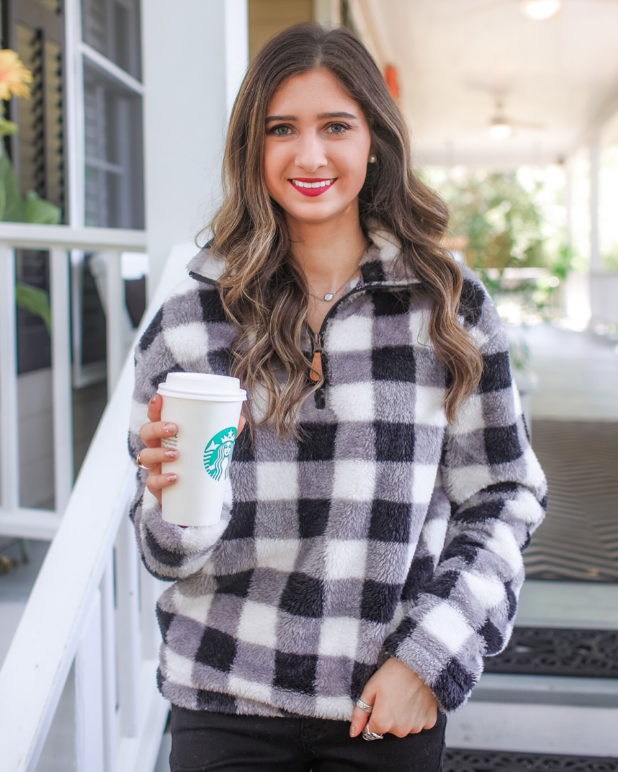 a long-sleeve fluffy pullover with a quarter zip, an adjustable bungee at the hem, and a foldable collar on a classic black and white buffalo plaid pattern fabric
