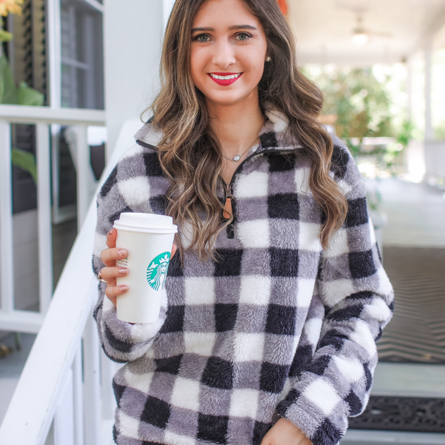 a long-sleeve fluffy pullover with a quarter zip, an adjustable bungee at the hem, and a foldable collar on a classic black and white buffalo plaid pattern fabric