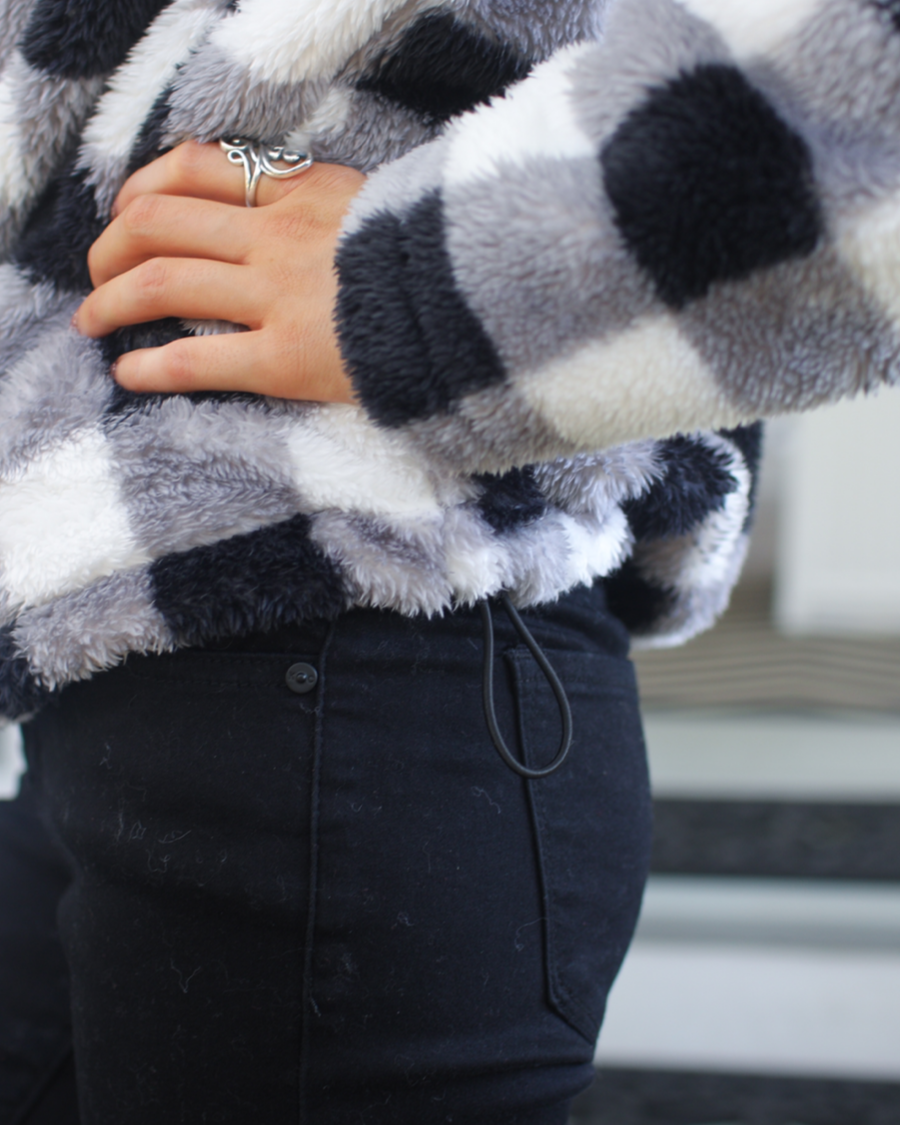 a long-sleeve fluffy pullover with a quarter zip, an adjustable bungee at the hem, and a foldable collar on a classic black and white buffalo plaid pattern fabric