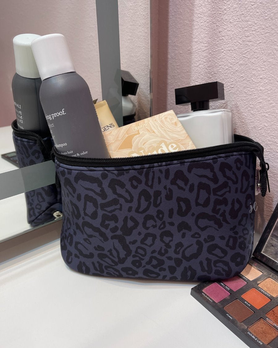 neoprene cosmetic bag in a black on black animal print pattern with dual top zippers (black) and expandable side snaps (silver) on a black on black leopard print pattern