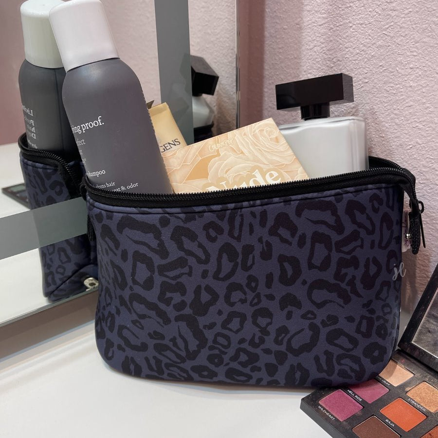 neoprene cosmetic bag in a black on black animal print pattern with dual top zippers (black) and expandable side snaps (silver) on a black on black leopard print pattern