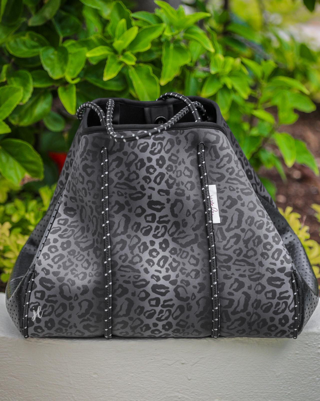 ultra-lightweight tote made of neoprene with a removable hard bottom liner, paracord shoulder straps, removable matching zippered pouch, magnetic side snap closures in silver hardware, and black interior (tote and pouch) on a black on black leopard print pattern