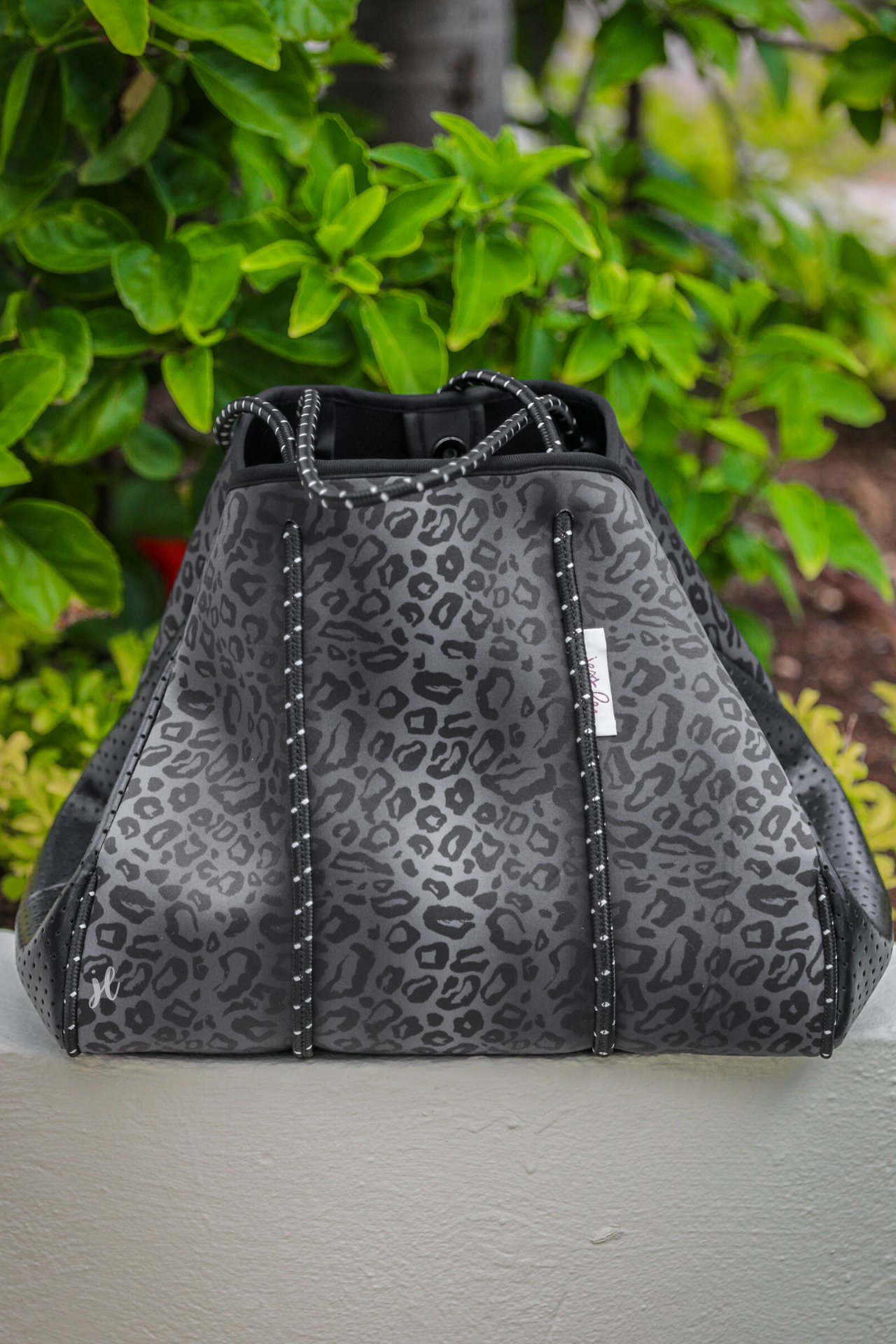 ultra-lightweight tote made of neoprene with a removable hard bottom liner, paracord shoulder straps, removable matching zippered pouch, magnetic side snap closures in silver hardware, and black interior (tote and pouch) on a black on black leopard print pattern