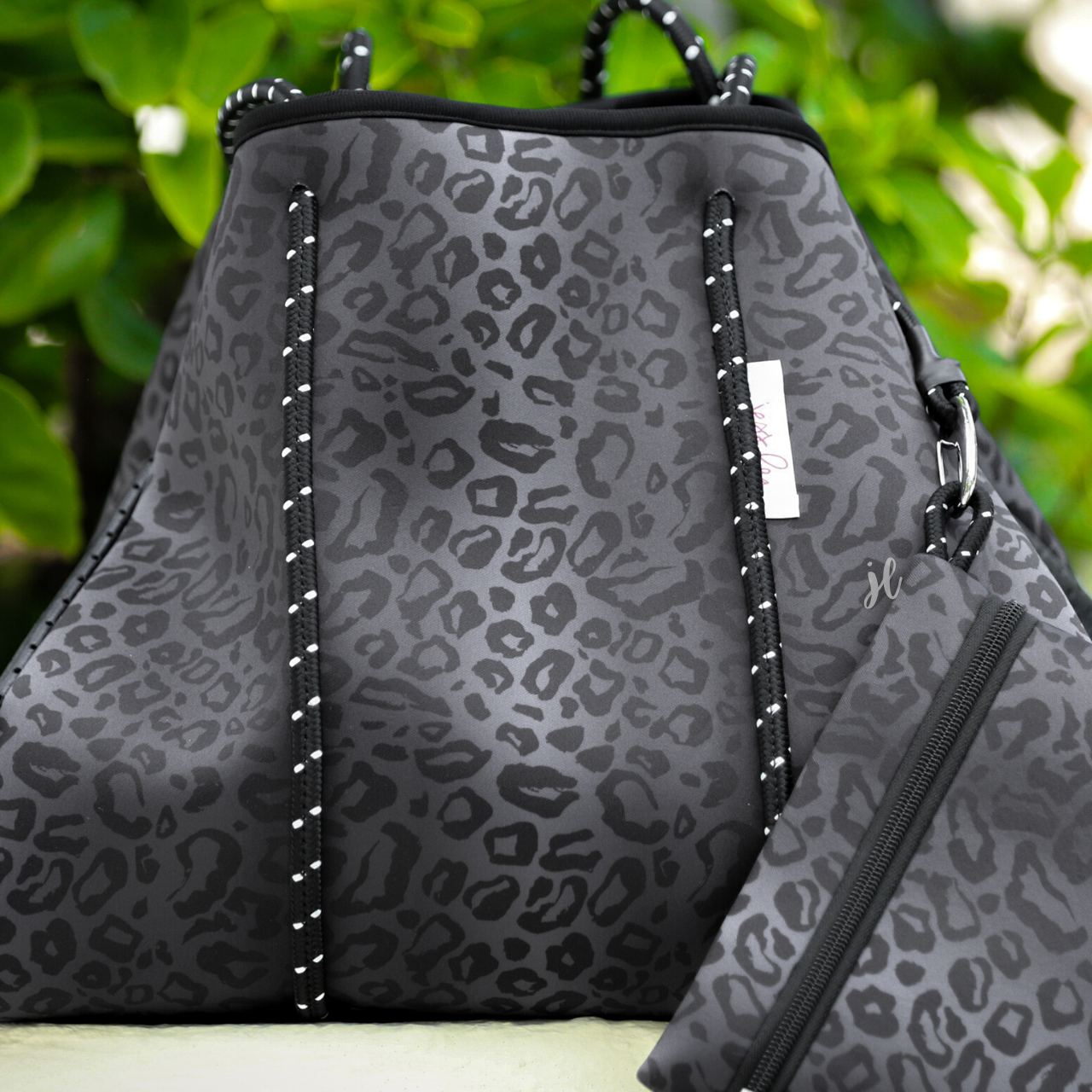 ultra-lightweight tote made of neoprene with a removable hard bottom liner, paracord shoulder straps, removable matching zippered pouch, magnetic side snap closures in silver hardware, and black interior (tote and pouch) on a black on black leopard print pattern