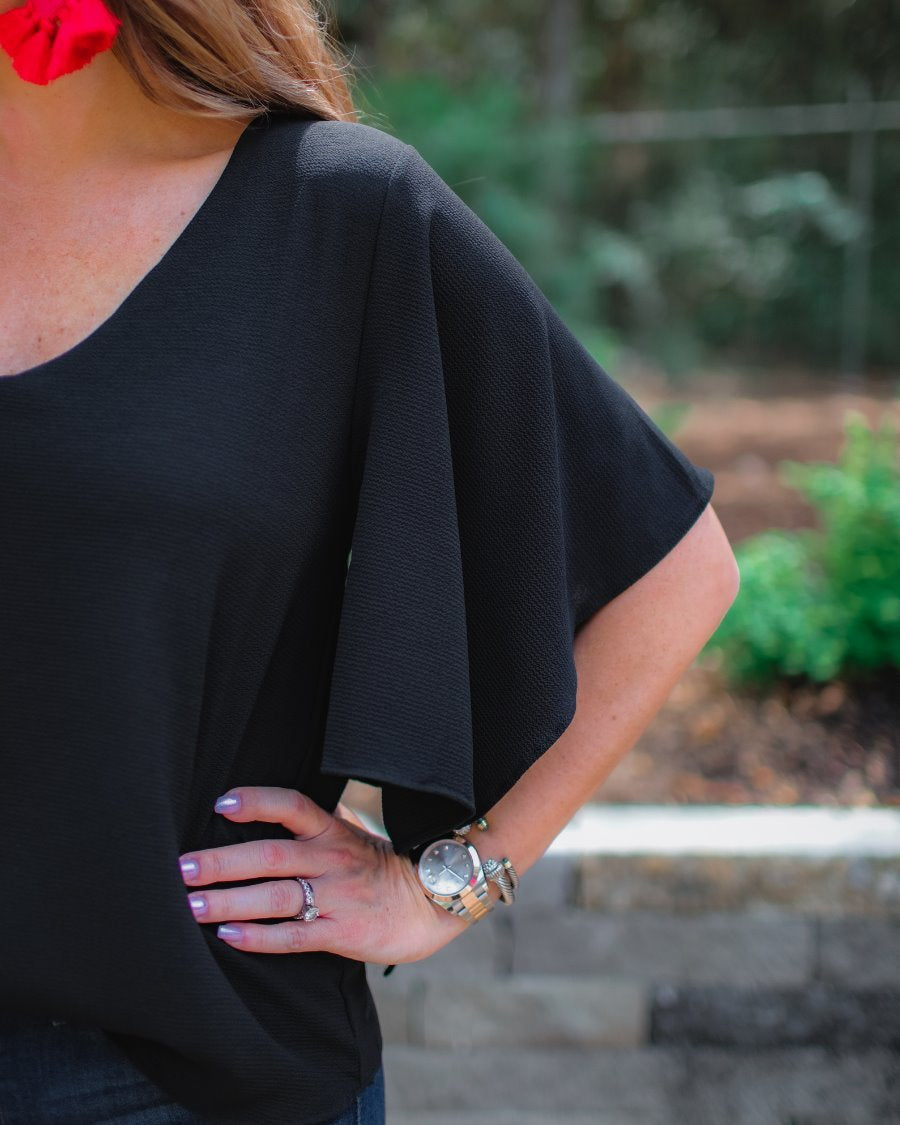 a black v-neck blouses crafted from lightweight textured fabric with asymmetrical half-flutter sleeves, front lining, and a relaxed fit