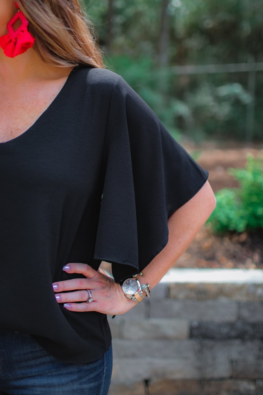 a black v-neck blouses crafted from lightweight textured fabric with asymmetrical half-flutter sleeves, front lining, and a relaxed fit