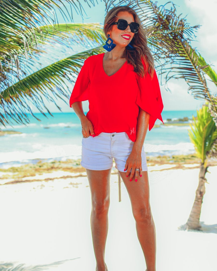 a red v-neck blouses crafted from lightweight textured fabric with asymmetrical half-flutter sleeves, front lining, and a relaxed fit, accented by a MADE IN USA watermark in the bottom left-hand corner