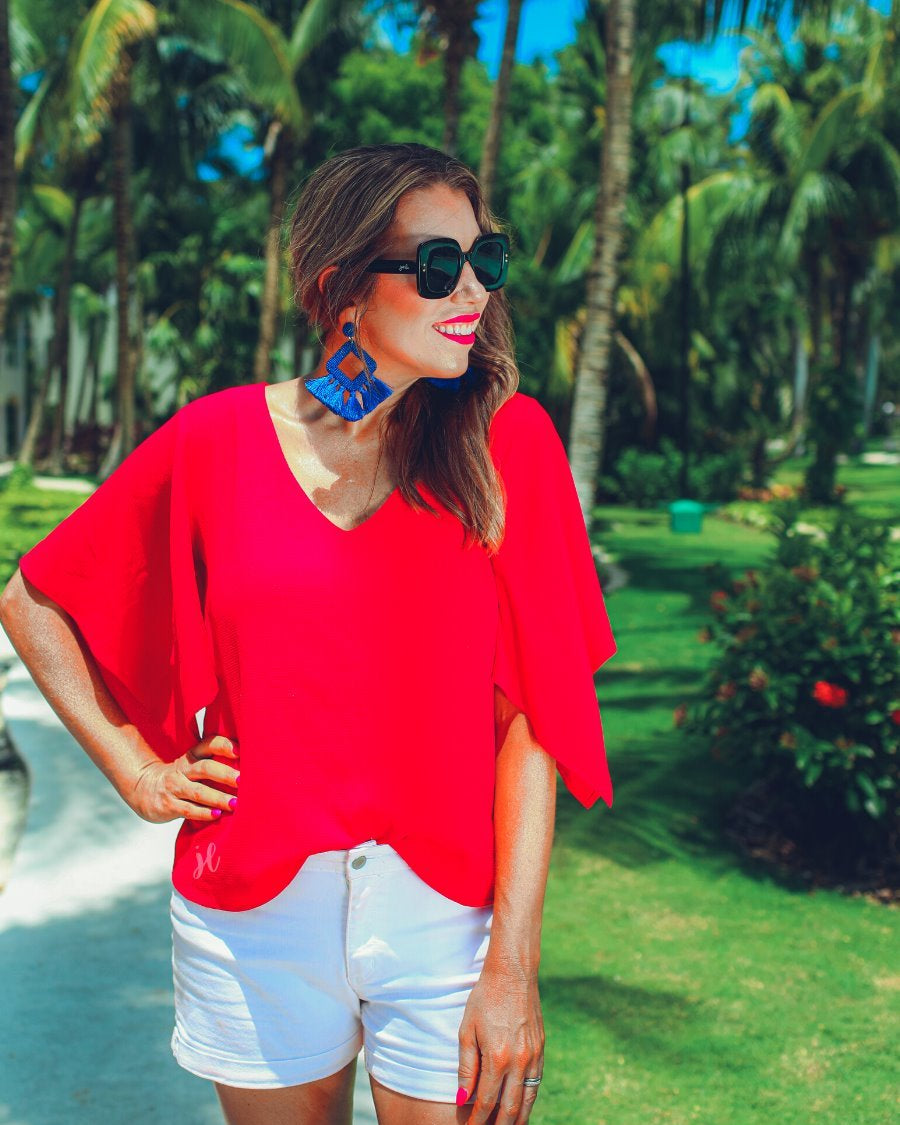 a red v-neck blouses crafted from lightweight textured fabric with asymmetrical half-flutter sleeves, front lining, and a relaxed fit, accented by a MADE IN USA watermark in the bottom left-hand corner