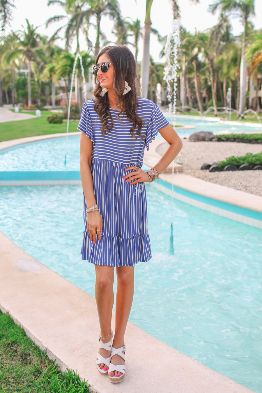 a blue striped babydoll dress with a rounded neckline, flutter ruffle sleeves, a tiered silhouette, a soft stretch fabric, and no lining