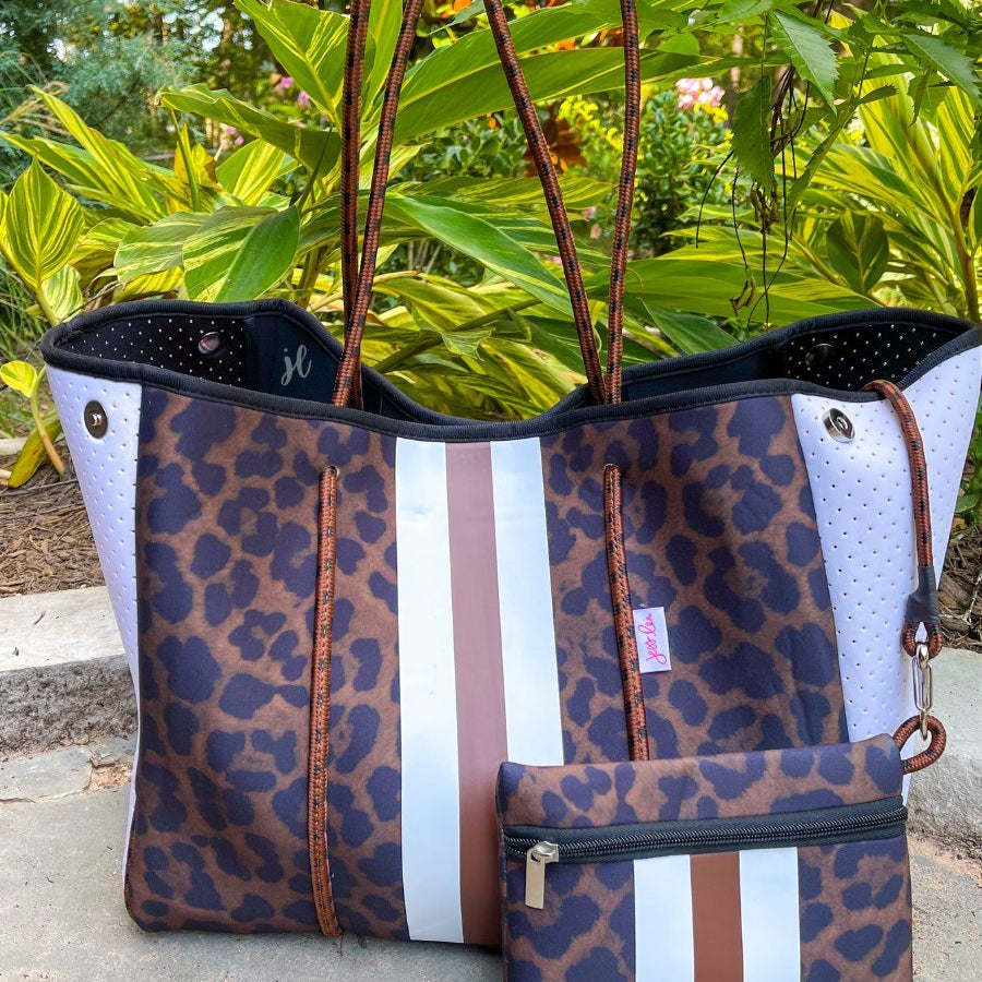 ultra-lightweight tote made of neoprene with a removable hard bottom liner, paracord shoulder straps, removable matching zippered pouch, magnetic side snap closures in silver hardware, black interior (tote and pouch), and racing stripes (brown and white) on a black and brown leopard print pattern
