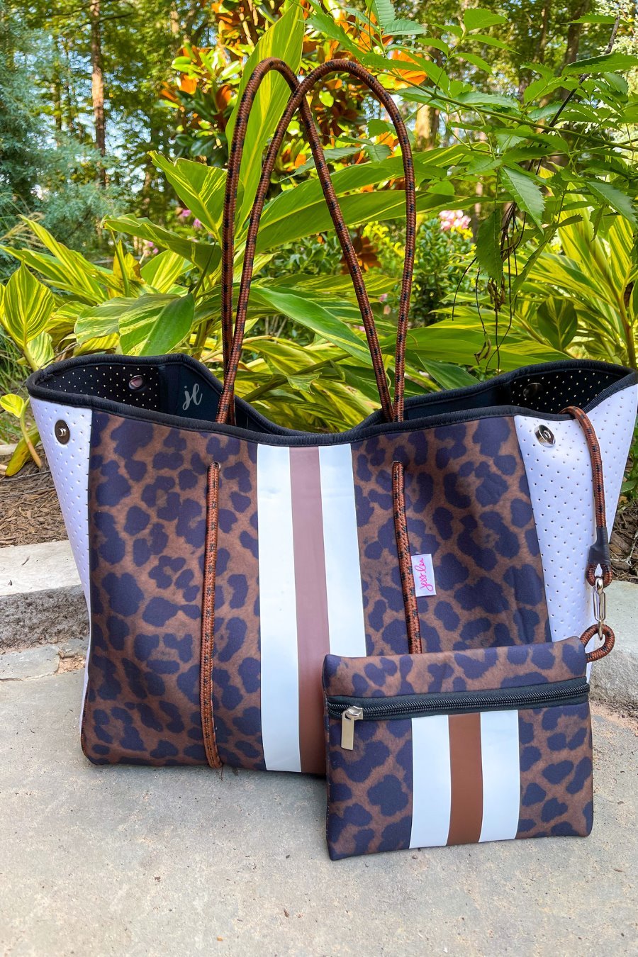 ultra-lightweight tote made of neoprene with a removable hard bottom liner, paracord shoulder straps, removable matching zippered pouch, magnetic side snap closures in silver hardware, black interior (tote and pouch), and racing stripes (brown and white) on a black and brown leopard print pattern