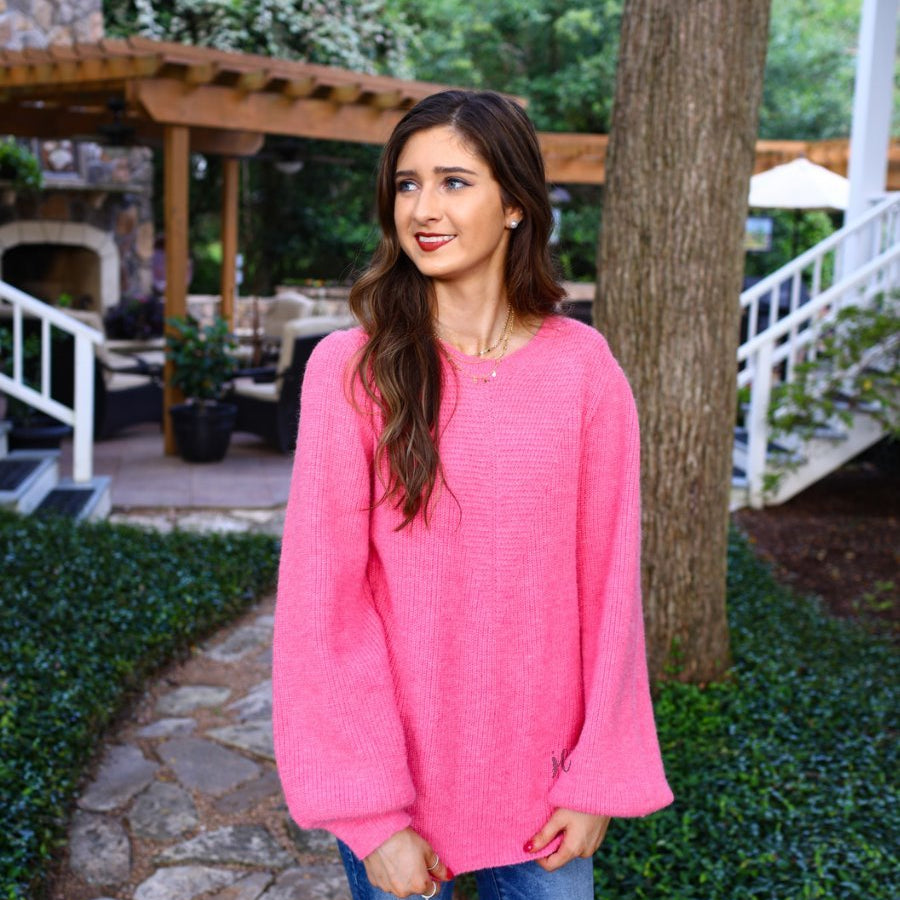 a pink soft knit long-sleeve sweater with a classic rounded neckline, statement balloon sleeves, and ribbed detailing at the cuffs and hemline