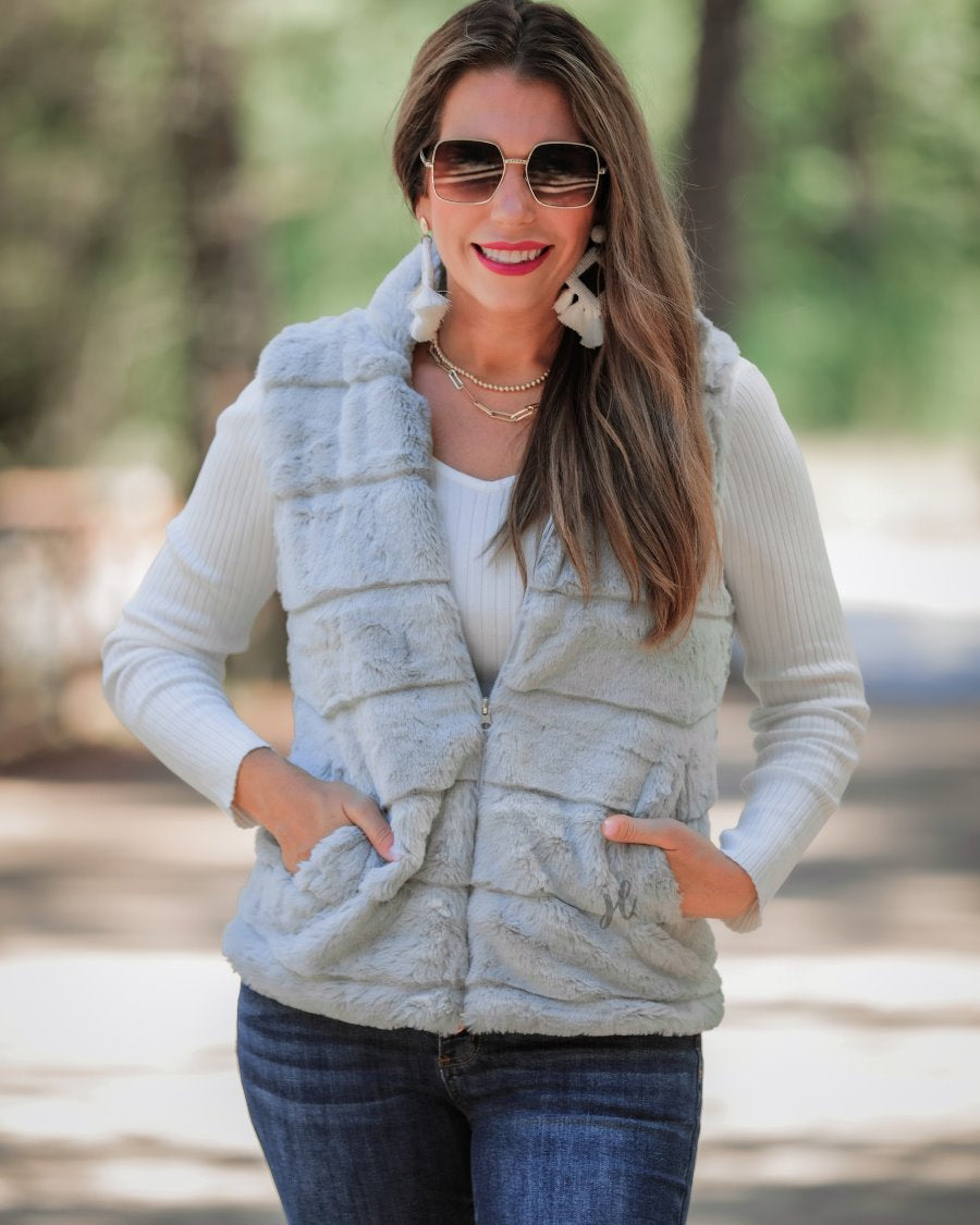 a sleeveless faux fur vest with a foldable collar, a front zip, sublte horizontal paneling, and front pockets made of super soft fabric that fits slightly oversized in grey