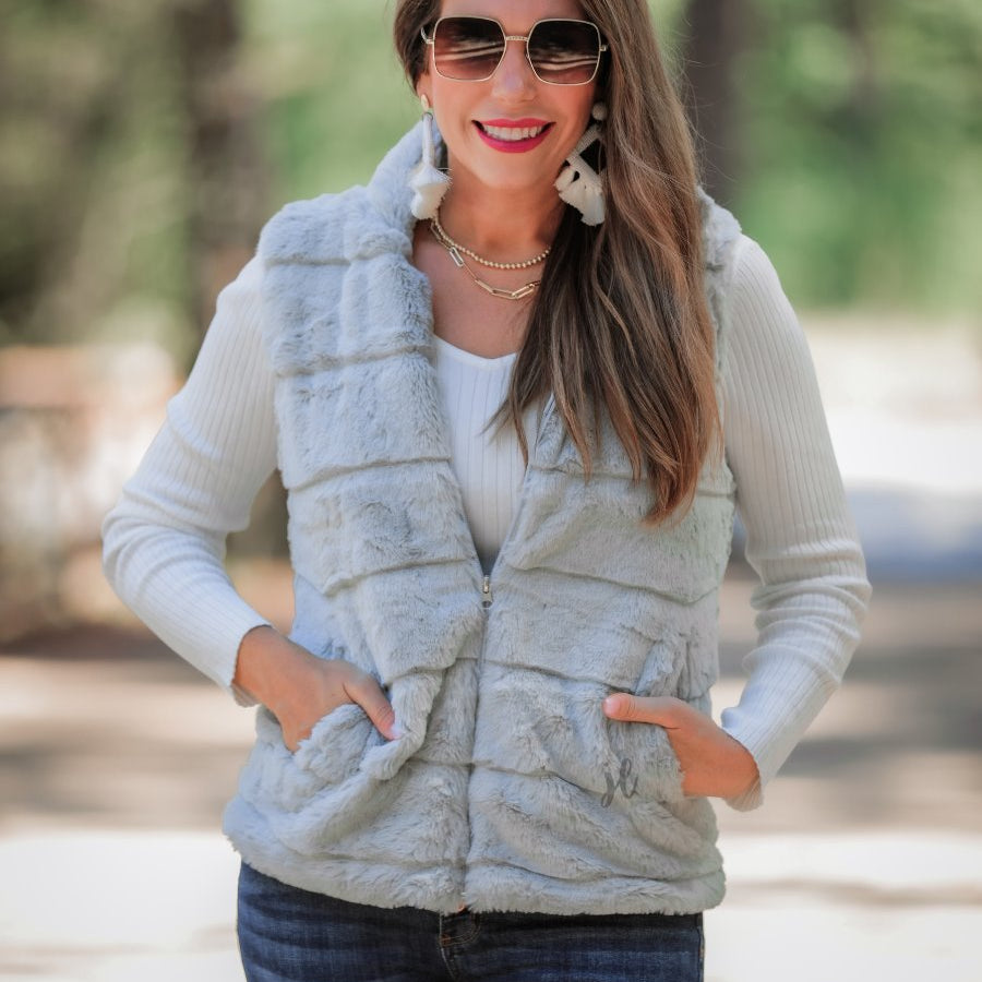 a sleeveless faux fur vest with a foldable collar, a front zip, sublte horizontal paneling, and front pockets made of super soft fabric that fits slightly oversized in grey