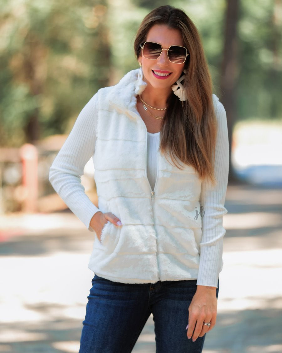 a sleeveless faux fur vest with a foldable collar, a front zip, sublte horizontal paneling, and front pockets made of super soft fabric that fits slightly oversized in white