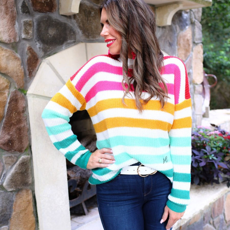 a textured knit long-sleeve sweater with a vibrant colorful stripe pattern (burgundy, magenta, mustard, teal, and forest green), a relaxed drop-shoulder fit, classic crew neckline, and ribbed detailing on the cuffs, neckline, and hemline on an ivory base