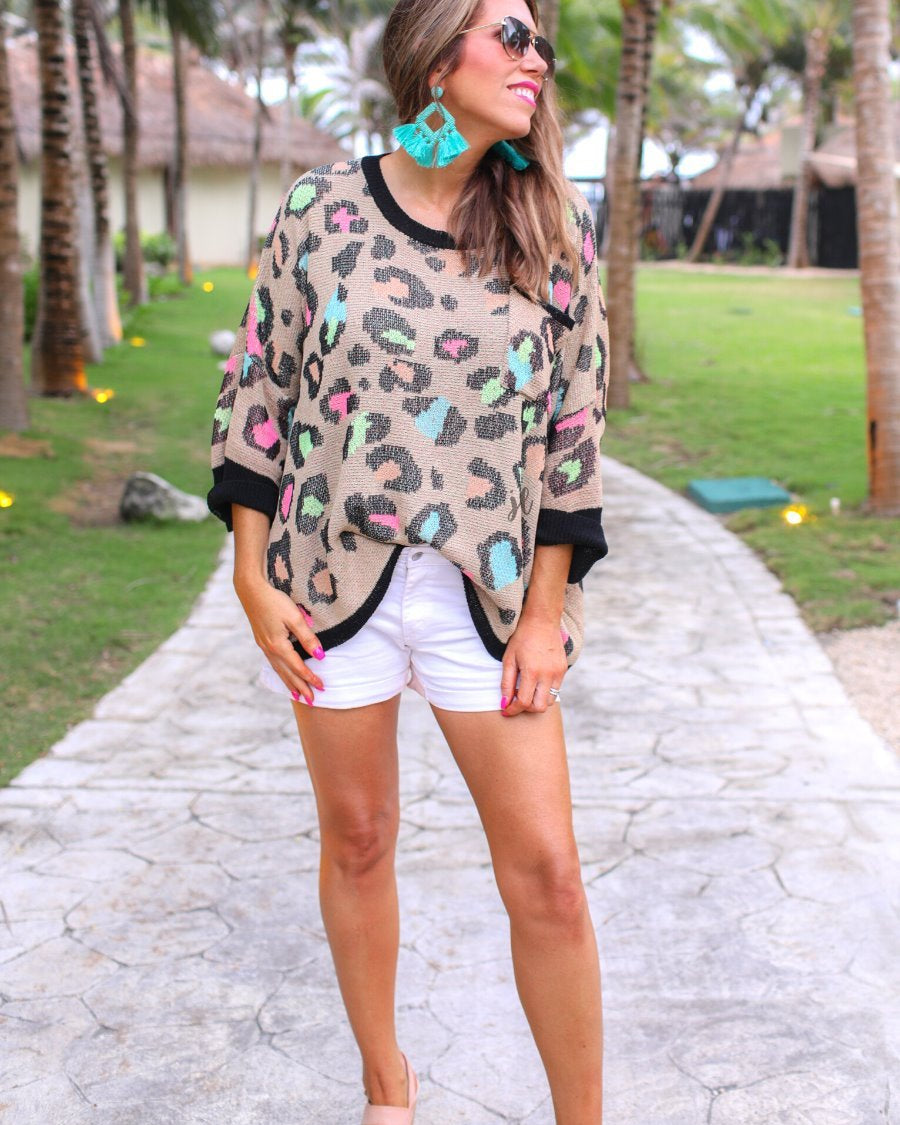 three quarter cuffed sleeve sweater made from unlined loose knit material with a rounded neckline, a chest pocket, and an oversized fit on a multicolor leopard pattern (blue, green, pink, and orange), a black accent color (chest pocket trim, cuffs, and hem), and a brown base