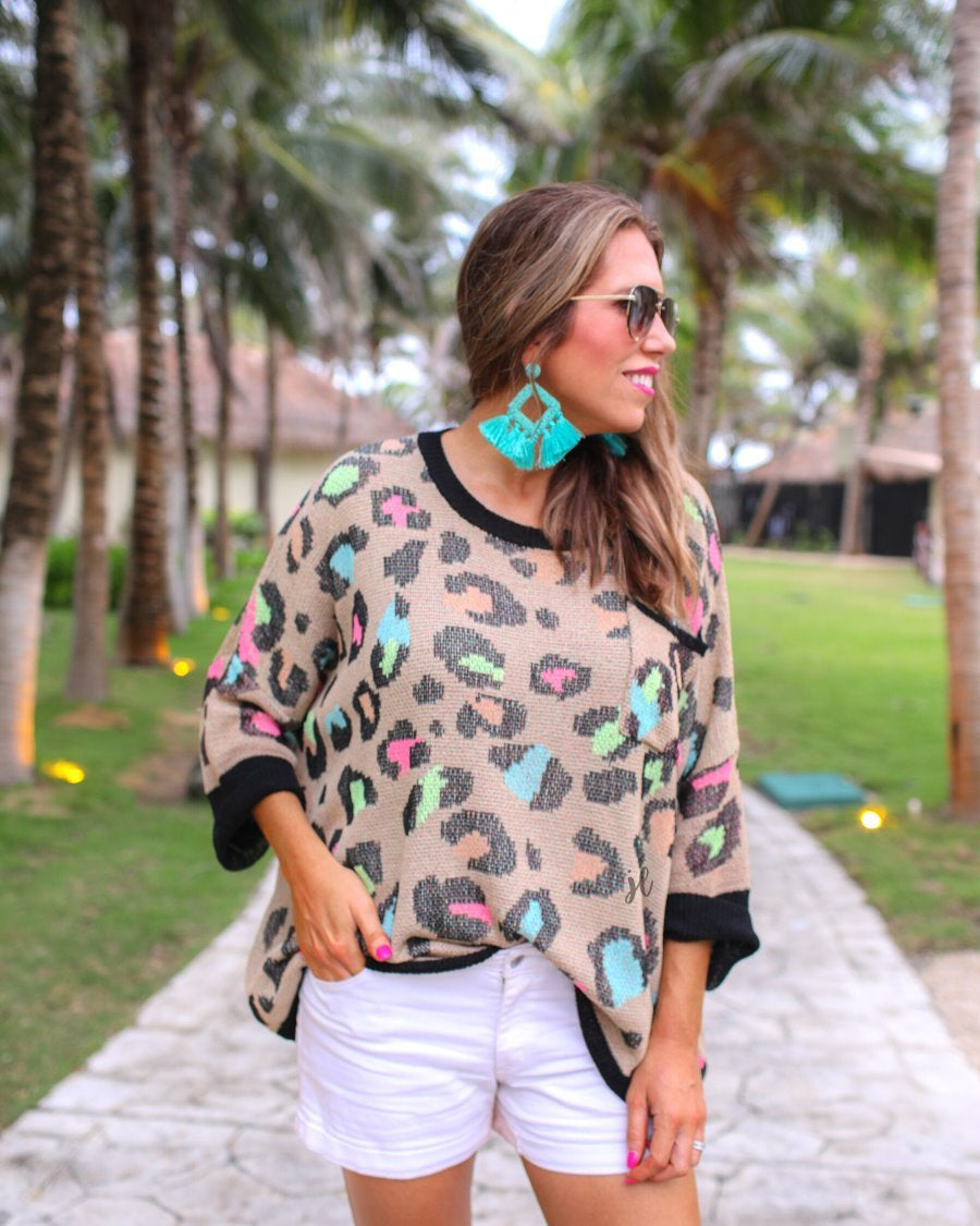 three quarter cuffed sleeve sweater made from unlined loose knit material with a rounded neckline, a chest pocket, and an oversized fit on a multicolor leopard pattern (blue, green, pink, and orange), a black accent color (chest pocket trim, cuffs, and hem), and a brown base