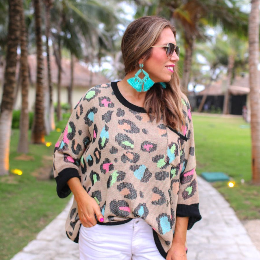 three quarter cuffed sleeve sweater made from unlined loose knit material with a rounded neckline, a chest pocket, and an oversized fit on a multicolor leopard pattern (blue, green, pink, and orange), a black accent color (chest pocket trim, cuffs, and hem), and a brown base