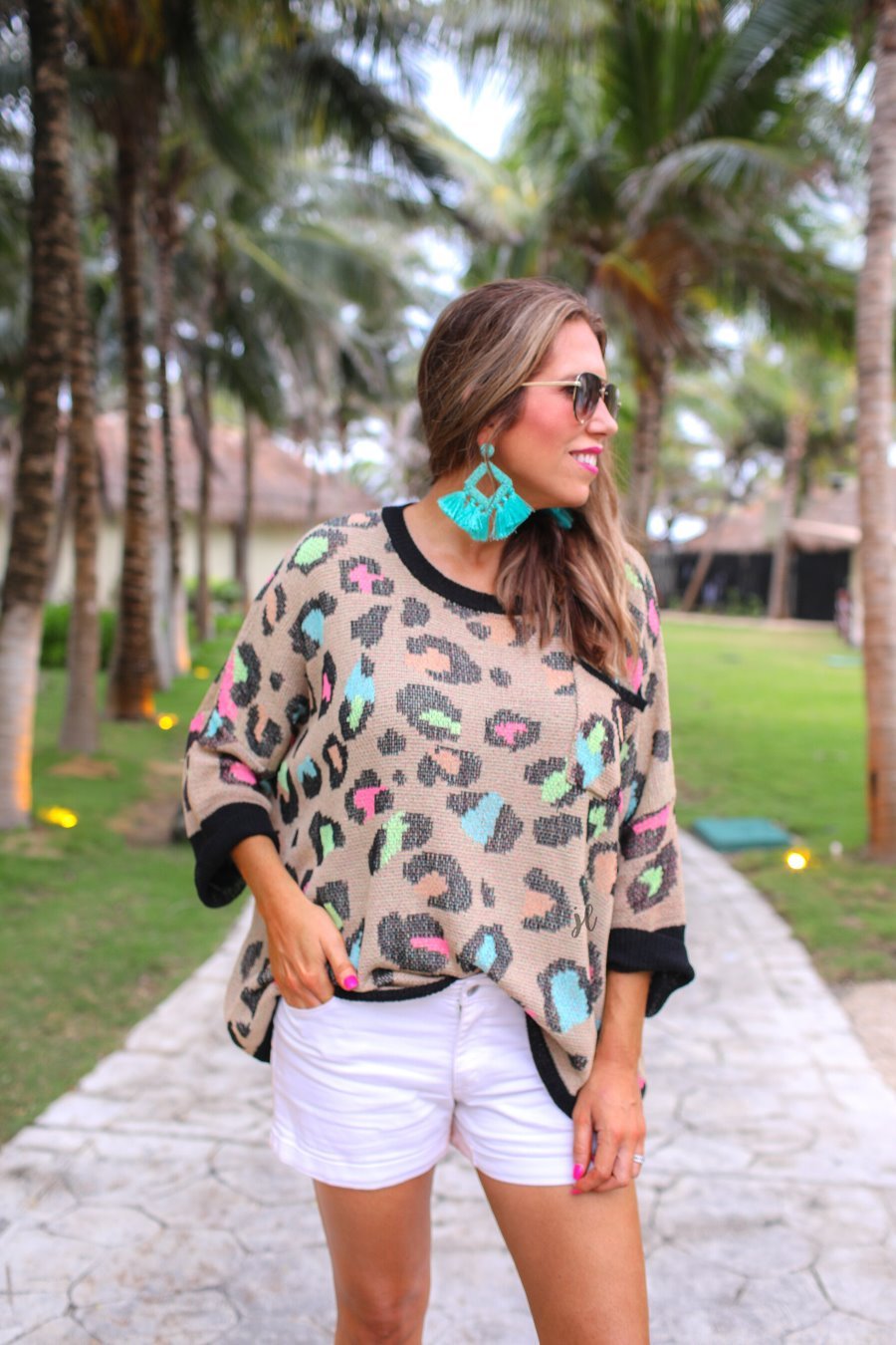 three quarter cuffed sleeve sweater made from unlined loose knit material with a rounded neckline, a chest pocket, and an oversized fit on a multicolor leopard pattern (blue, green, pink, and orange), a black accent color (chest pocket trim, cuffs, and hem), and a brown base