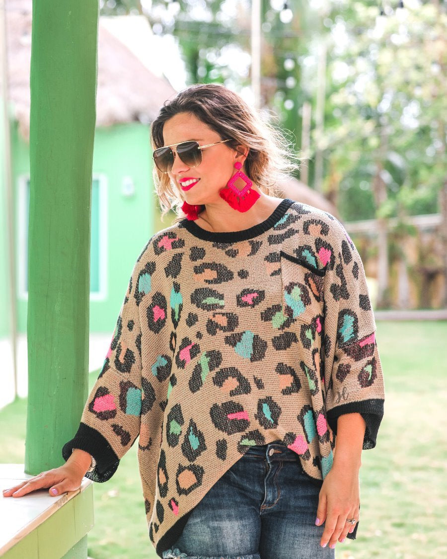 three quarter cuffed sleeve sweater made from unlined loose knit material with a rounded neckline, a chest pocket, and an oversized fit on a multicolor leopard pattern (blue, green, pink, and orange), a black accent color (chest pocket trim, cuffs, and hem), and a brown base