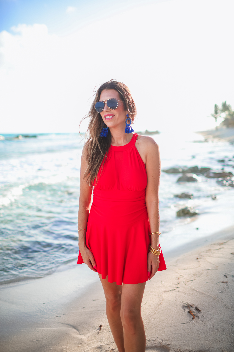 a solid red one-piece swimsuit with a halter neckline, sheer mesh V-detail, secure back clasp, removable padding, skirted hem, and attached full-coverage bottoms